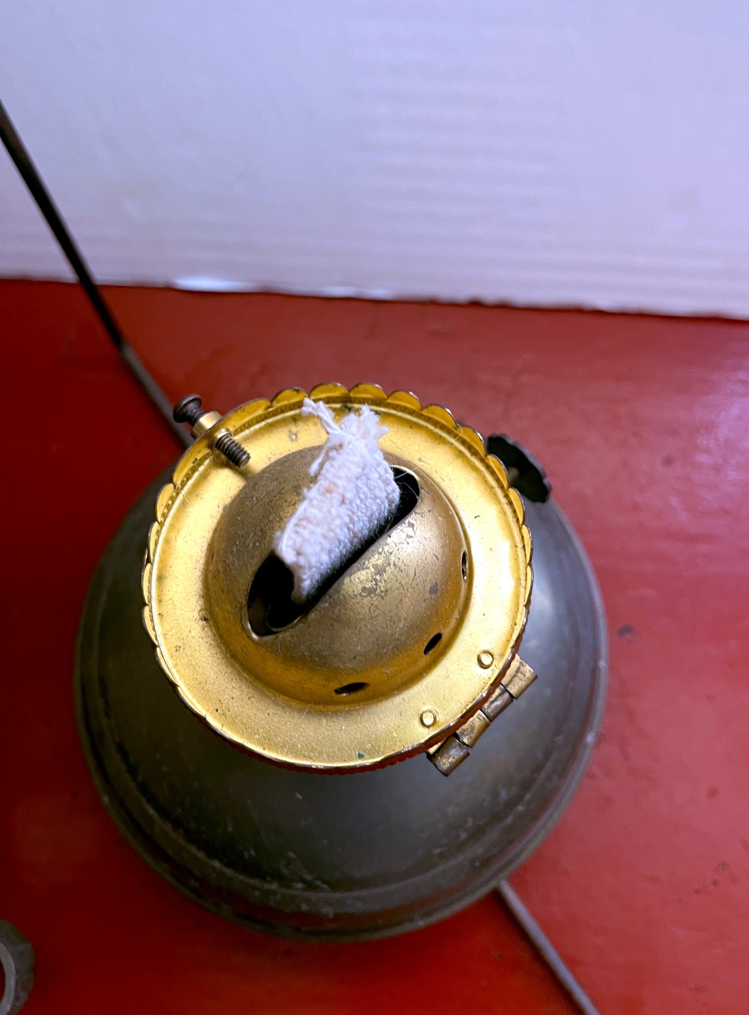 Close-up of a vintage oil lamp with a brass top on a red surface.