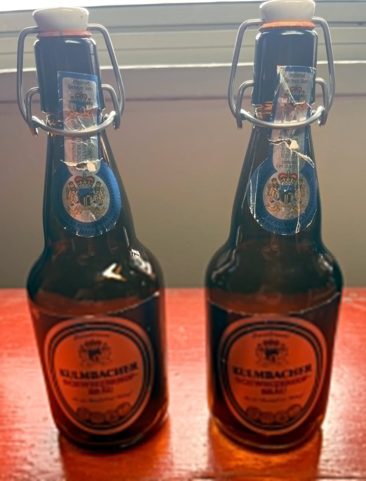 Two Kulmbacher beer bottles on a wooden surface with a blurred background