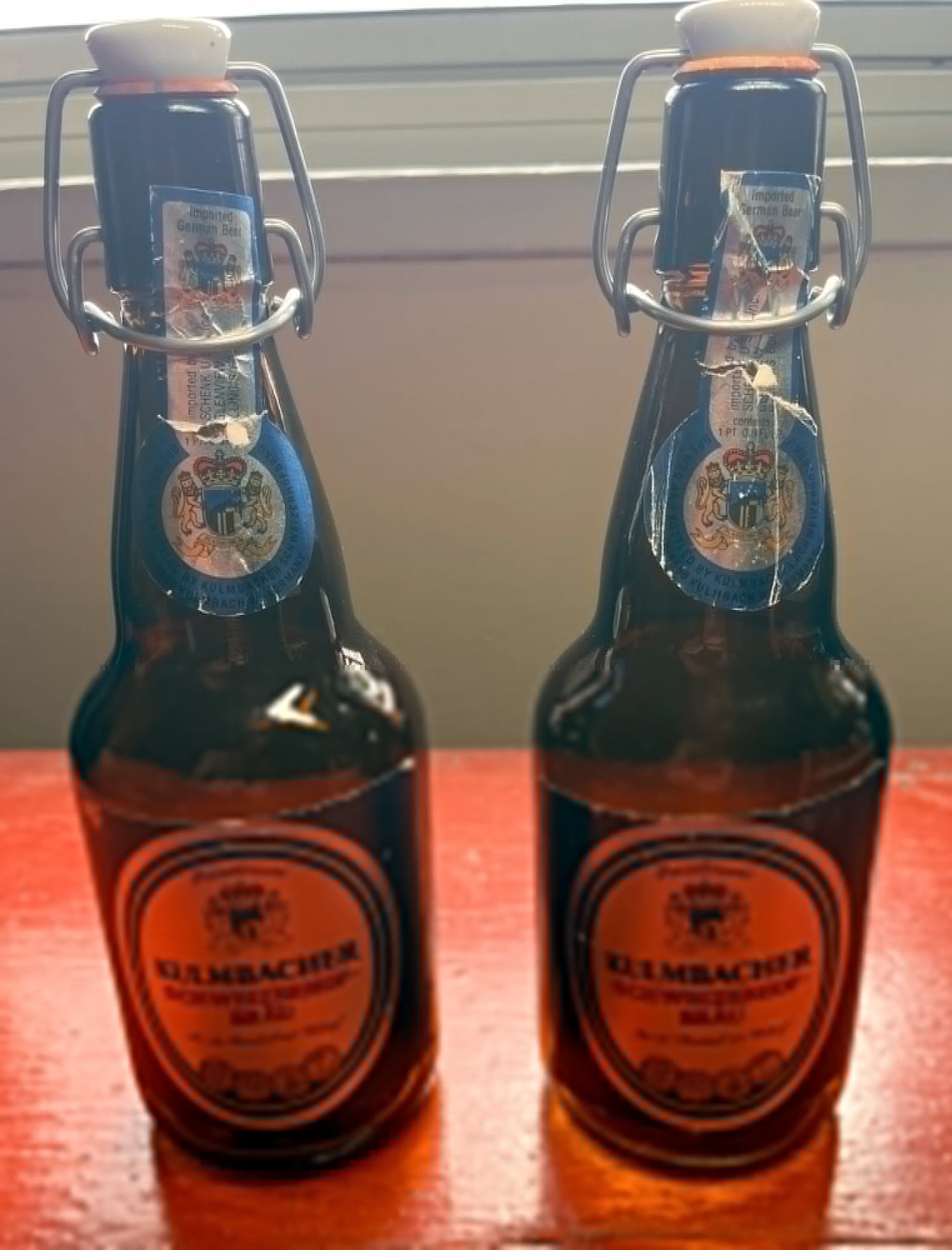 Two Kulmbacher beer bottles on a wooden surface with a blurred background