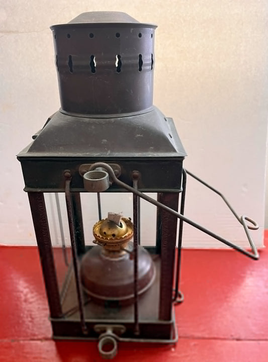 Vintage-style lantern with a dark gray top and brown base on a red surface.